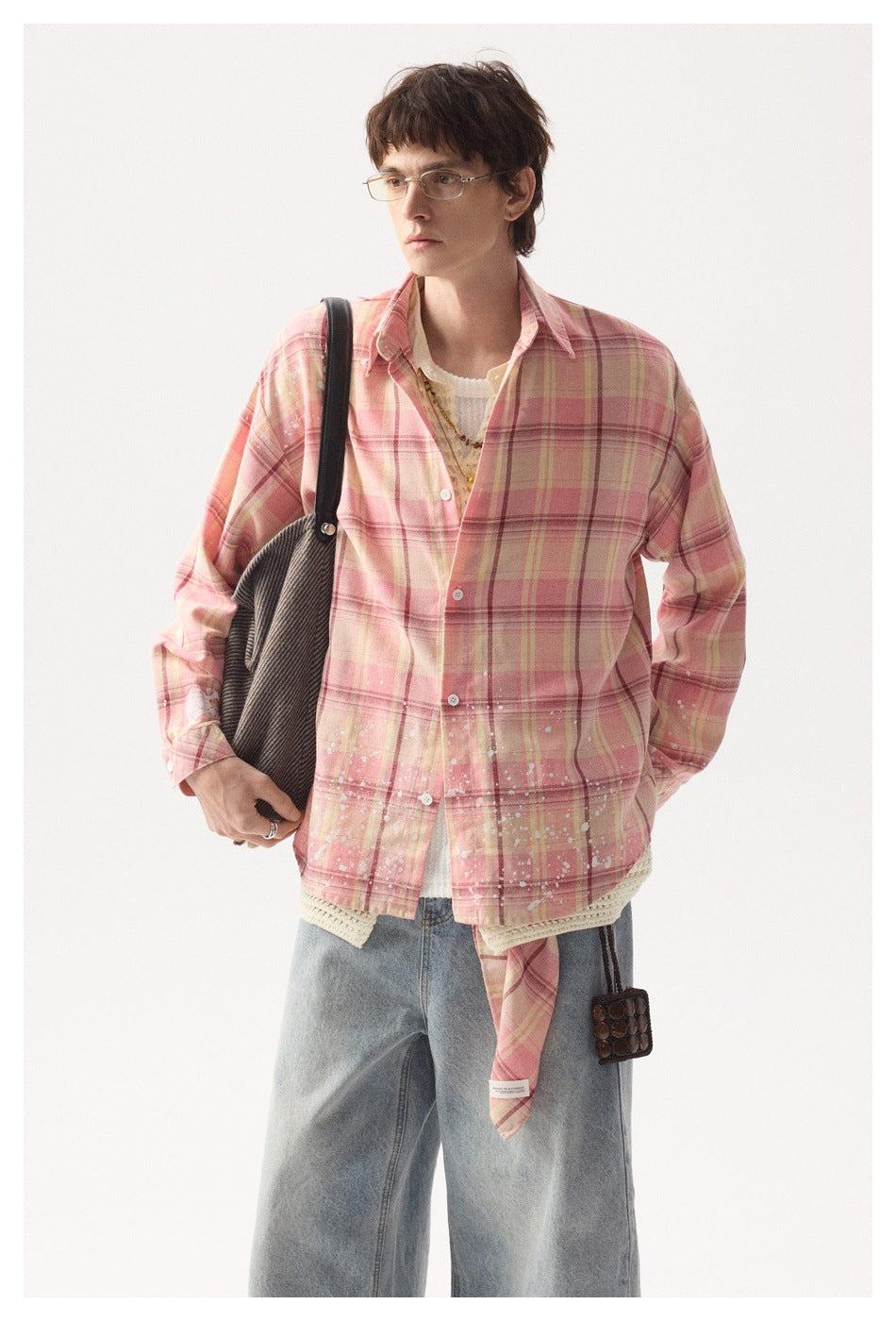 Model in a pink plaid button-front overshirt with white splatter details, layered over cream knitwear.