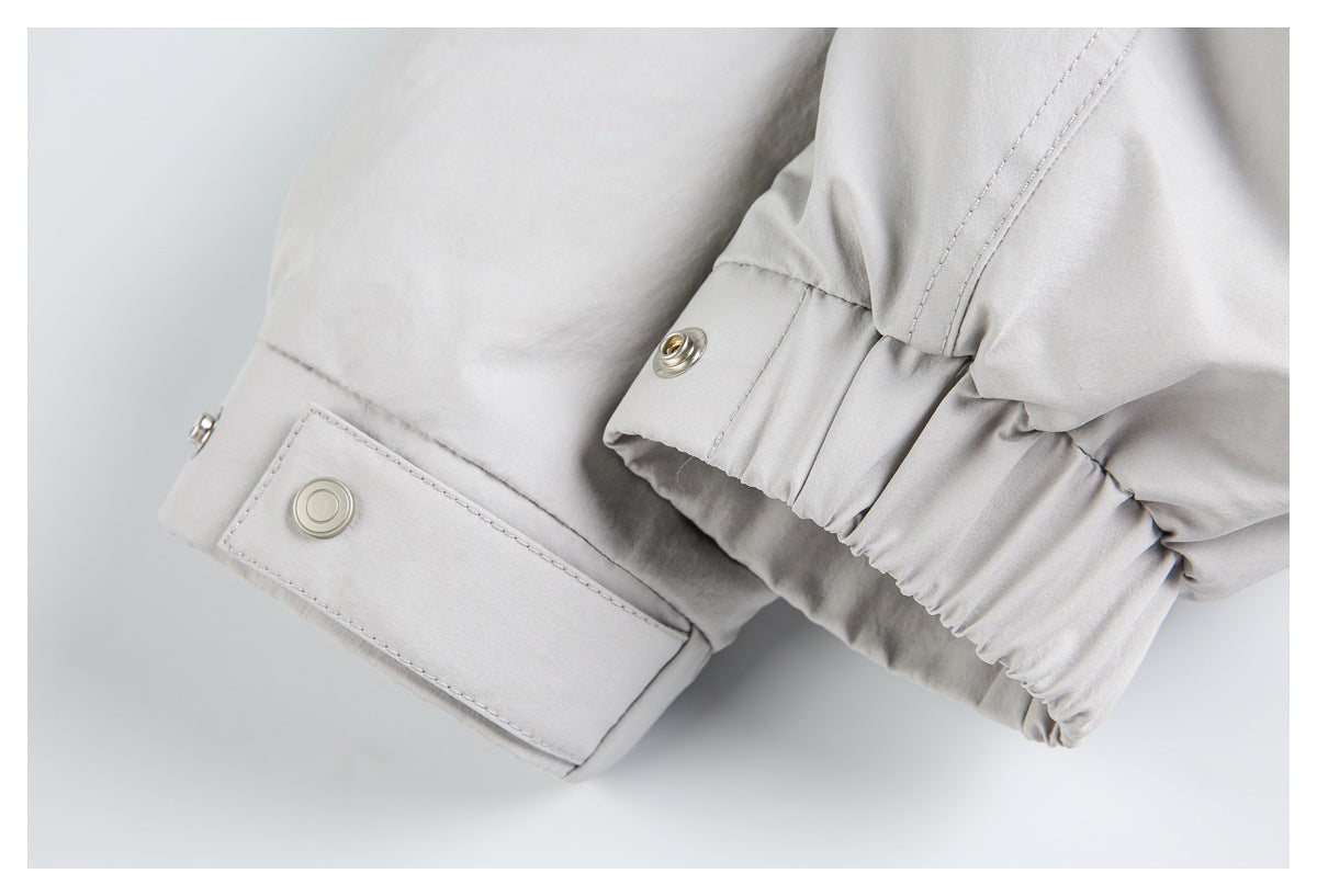 Close-up of a pale gray sleeve cuff with snap tabs, stitching, and gathered elastic.