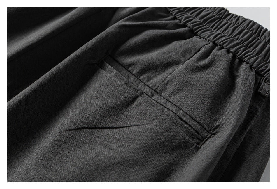 Close-up of dark pants showing a welt pocket beneath the gathered elastic waistband.