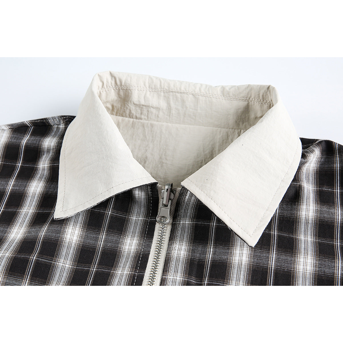 Close-up of a cream pointed collar and front zipper on a black-and-white plaid jacket.