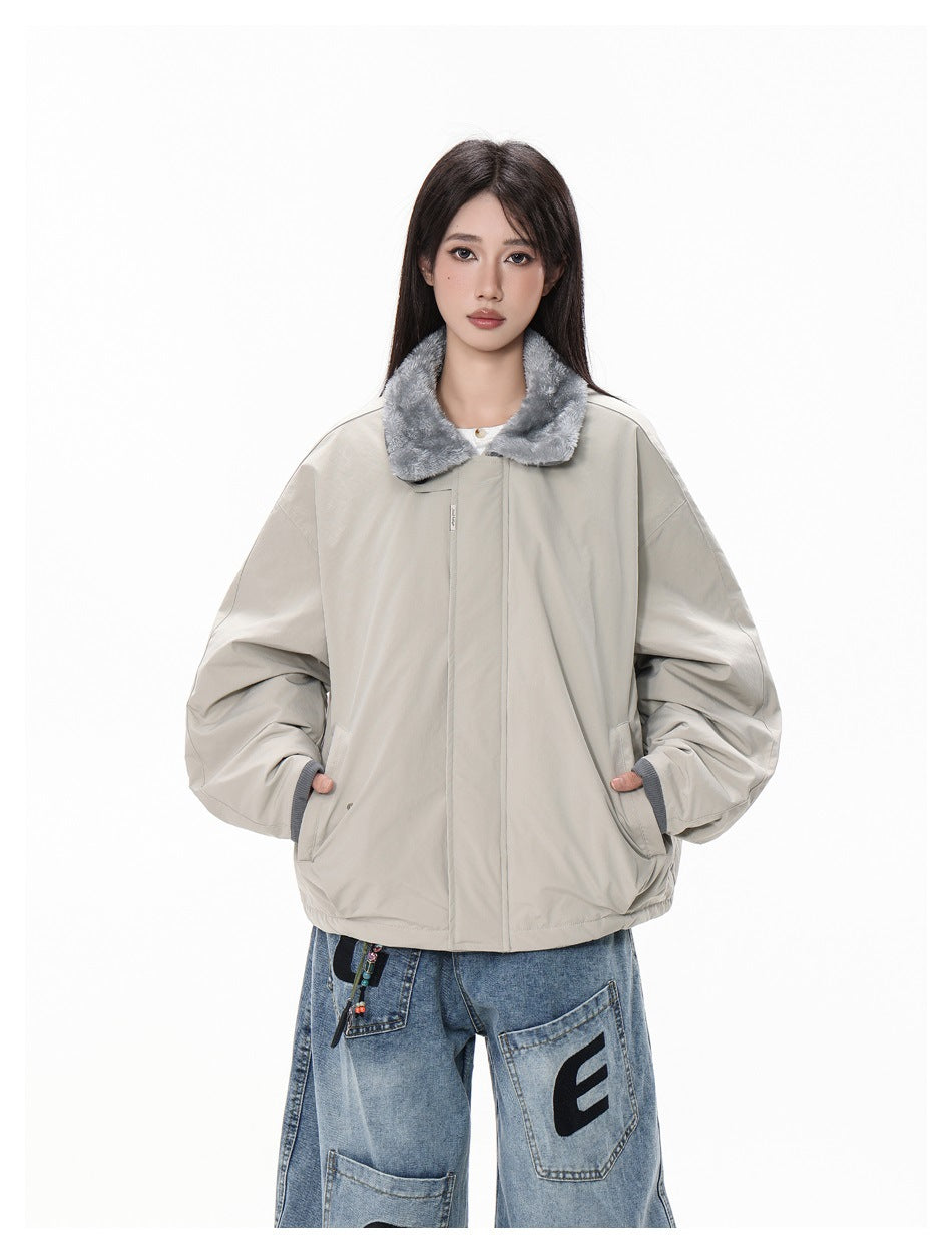 Model wearing a light gray oversized jacket with a gray plush collar and blue patchwork jeans, hands in pockets.