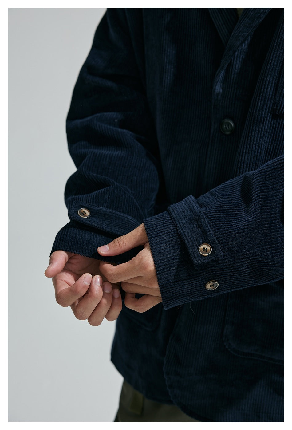 Close-up of a person adjusting the cuff of a dark navy corduroy jacket with buttoned sleeve tabs.