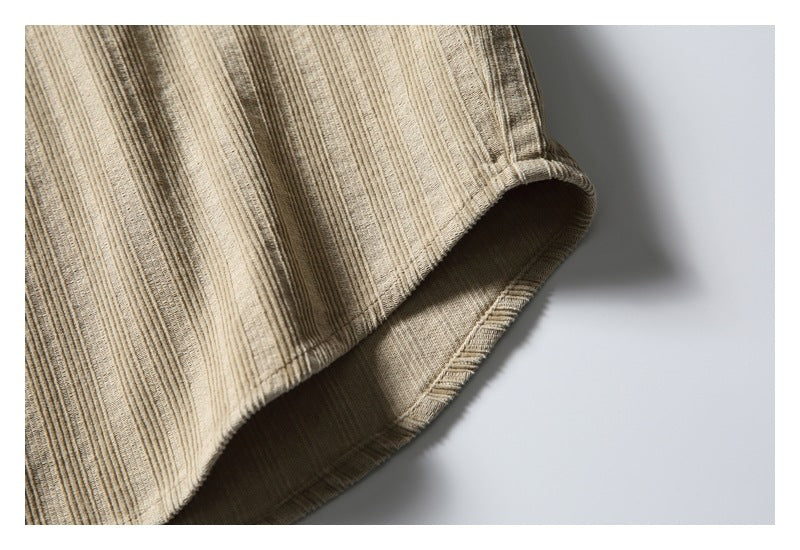 Close-up of the tan shirt's curved hem and stitched edge against a pale background.