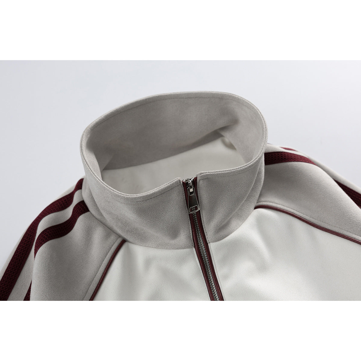 Close-up of a light gray stand collar and front zipper on a white jacket with burgundy trim.