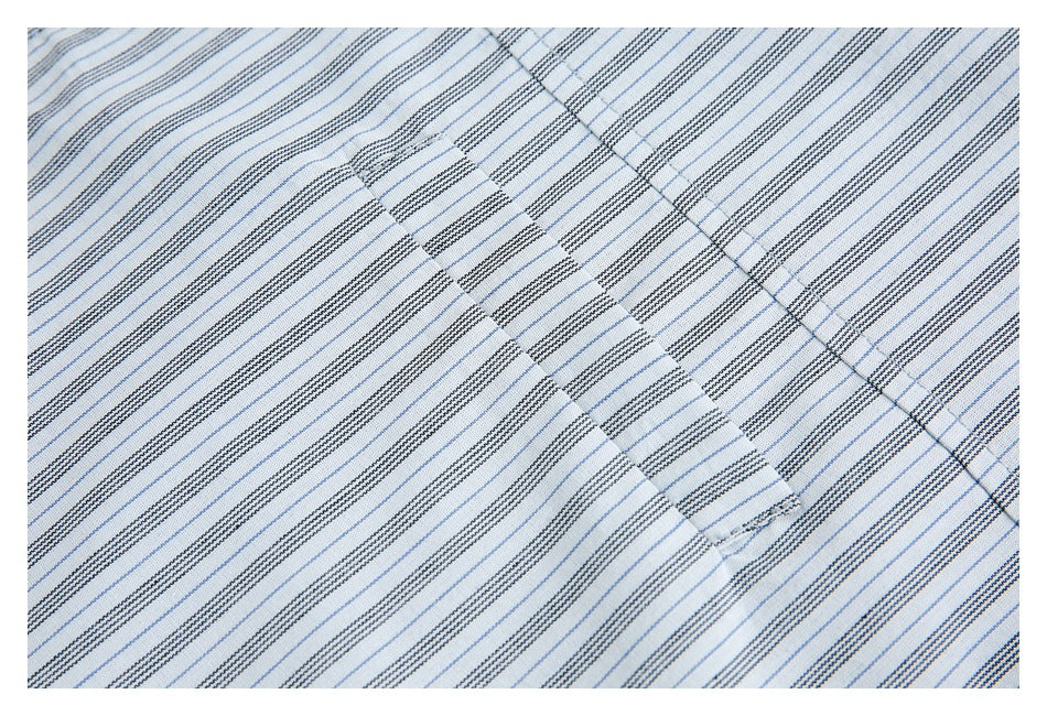 Close-up of white fabric with fine blue and dark stripes and a stitched overlapping panel.