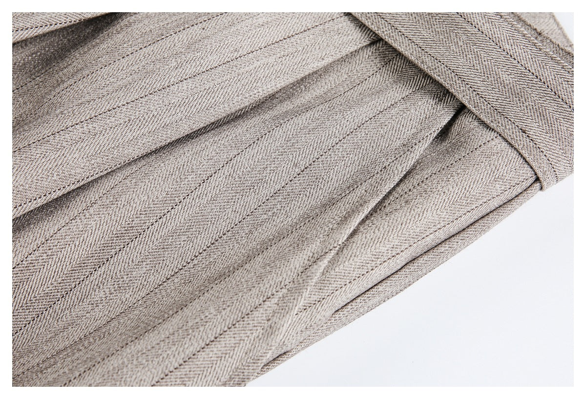 Close-up of taupe-gray herringbone trousers showing stitched pleats and overlapping fabric panels.