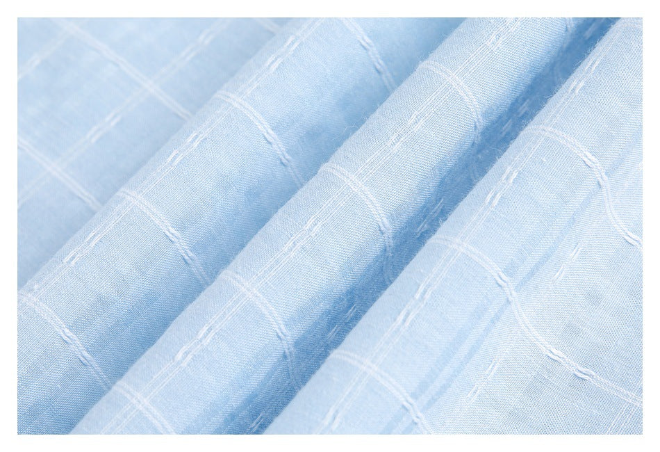 Macro view of pale blue fabric draped in folds, featuring a raised white grid pattern.