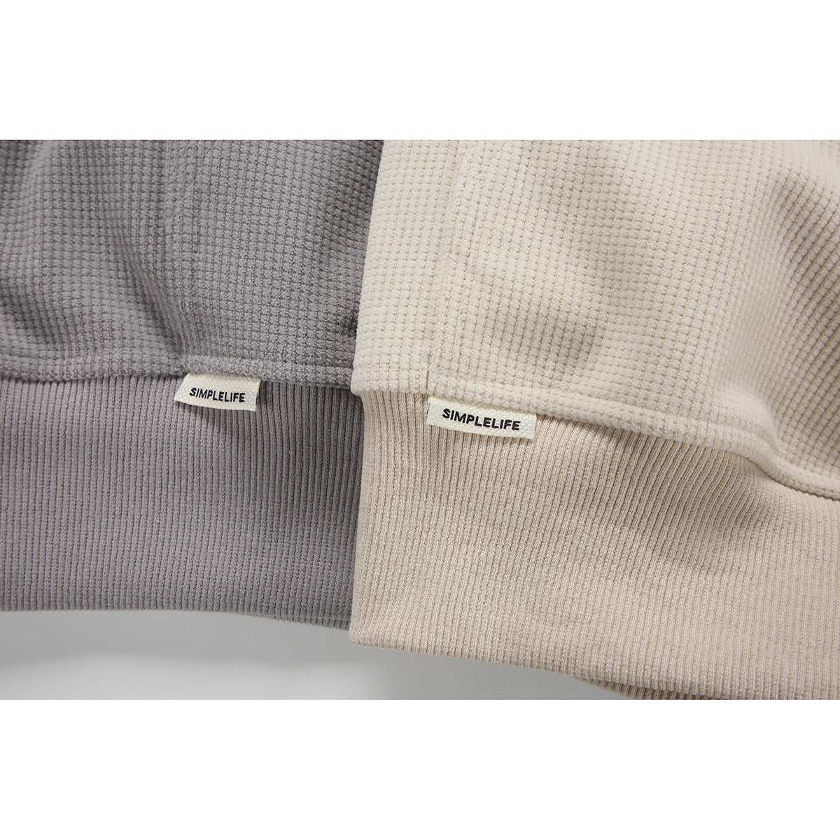 Close-up of gray and cream pullover hems with ribbed bands and sewn SIMPLELIFE labels.