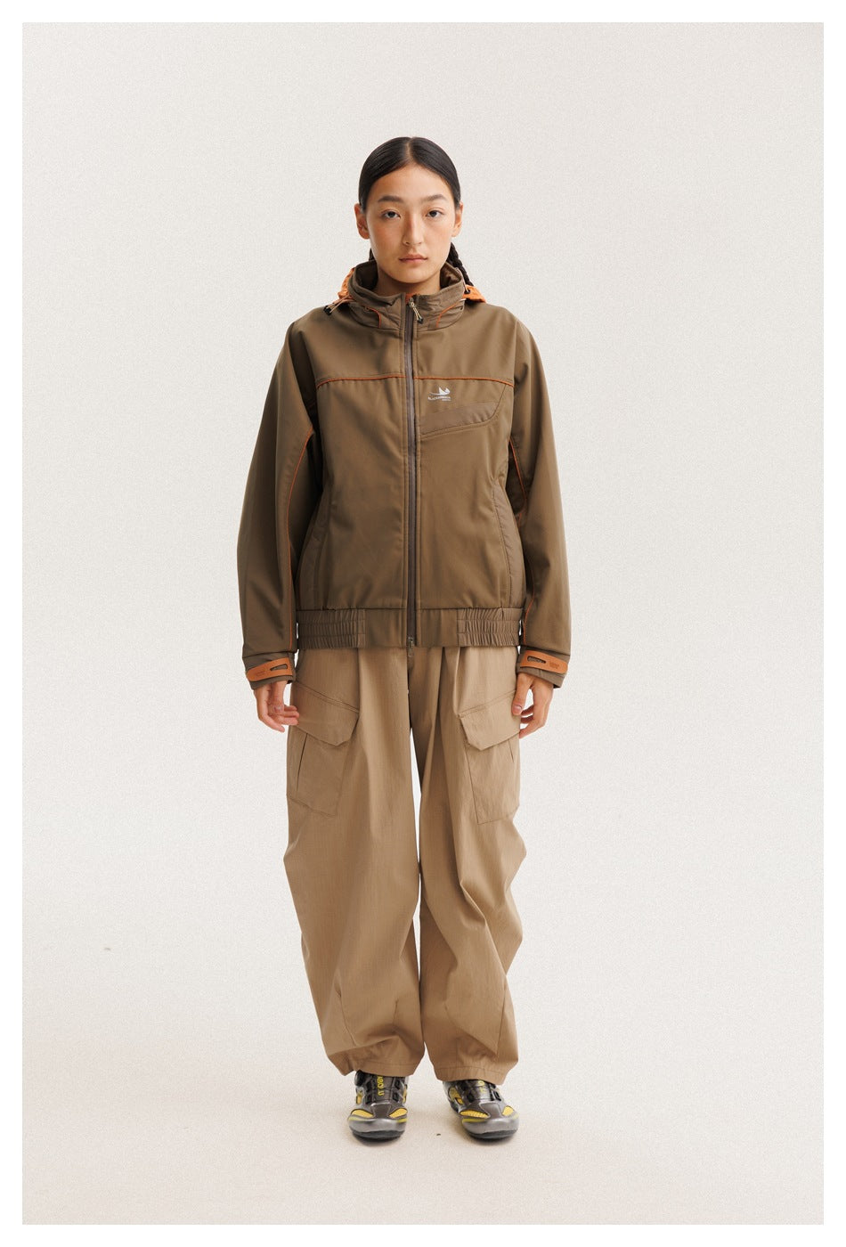Model wearing a brown hooded zip jacket with orange trim and tan cargo pants, shown full length from the front.