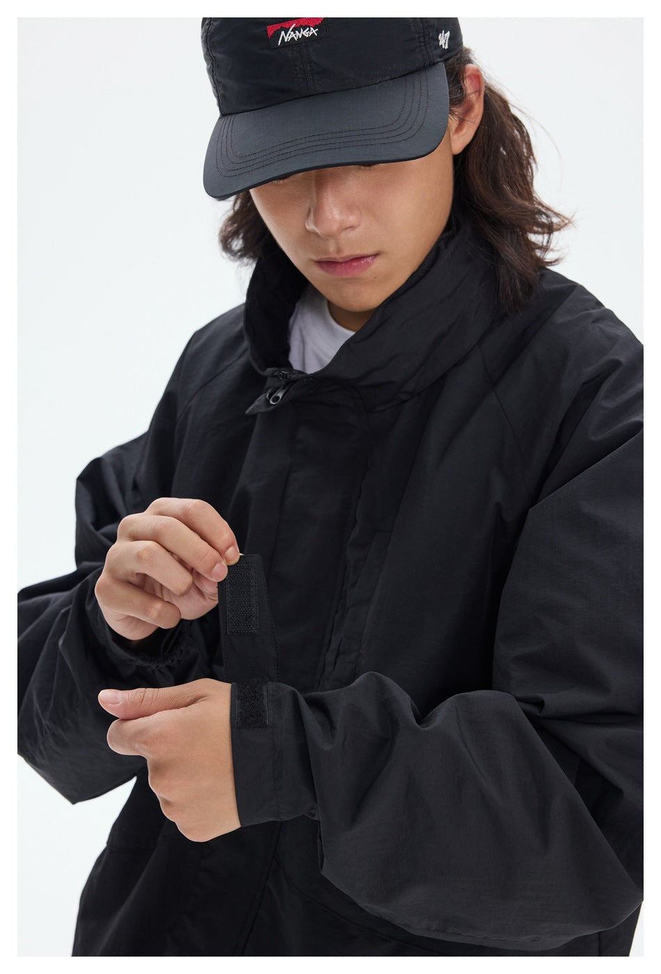 Close-up of a black jacket’s high collar and adjustable hook-and-loop cuff, worn by a model.