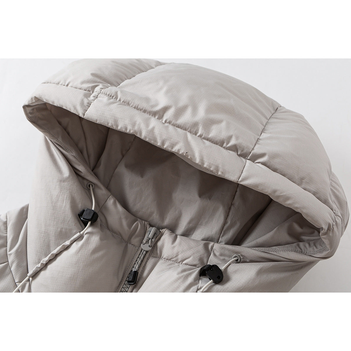 Close-up of a light taupe puffer jacket hood, showing padded panels, drawcords, and the top of the front zipper.