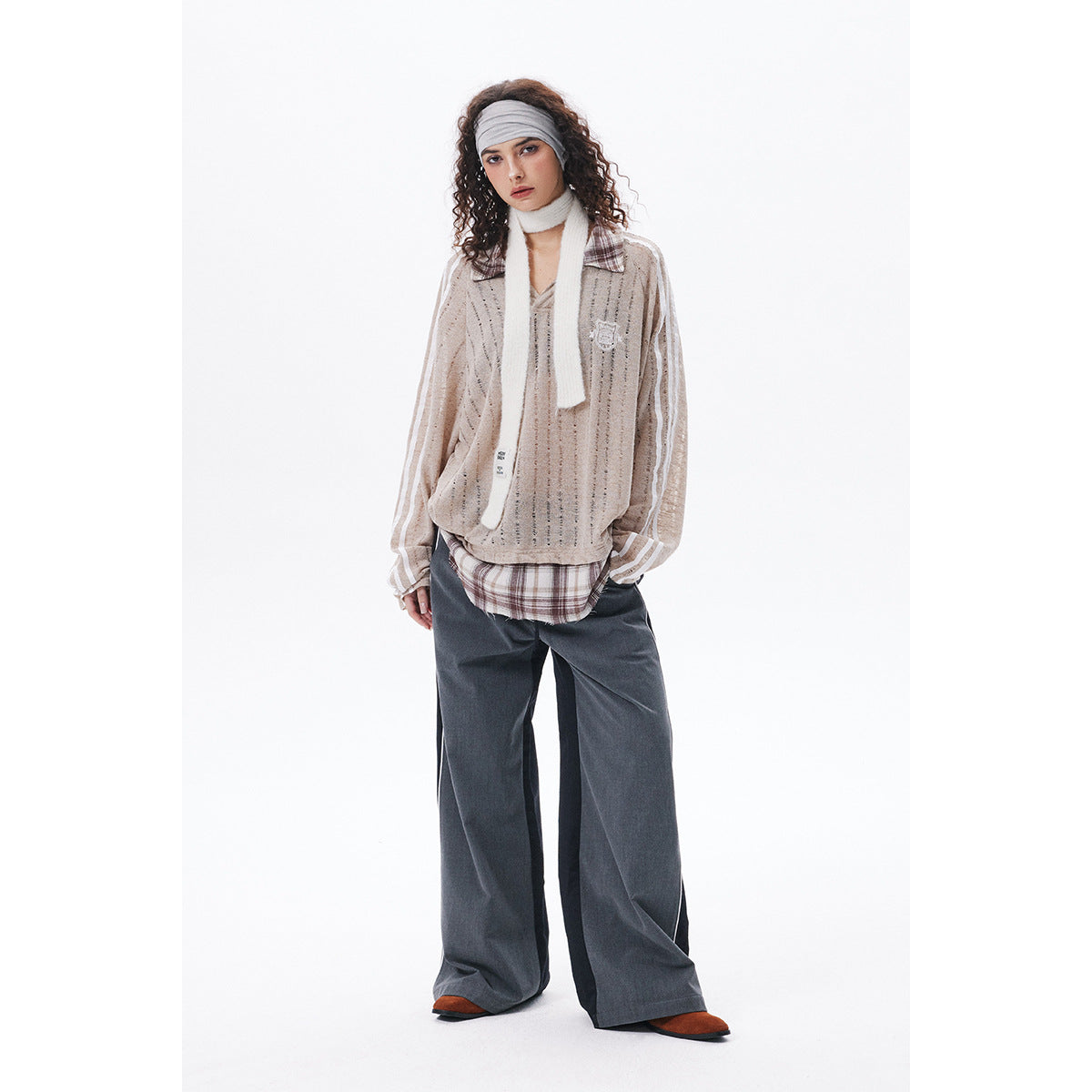 Model wearing a taupe open-knit striped polo sweater with plaid collar, scarf and wide-leg charcoal trousers.