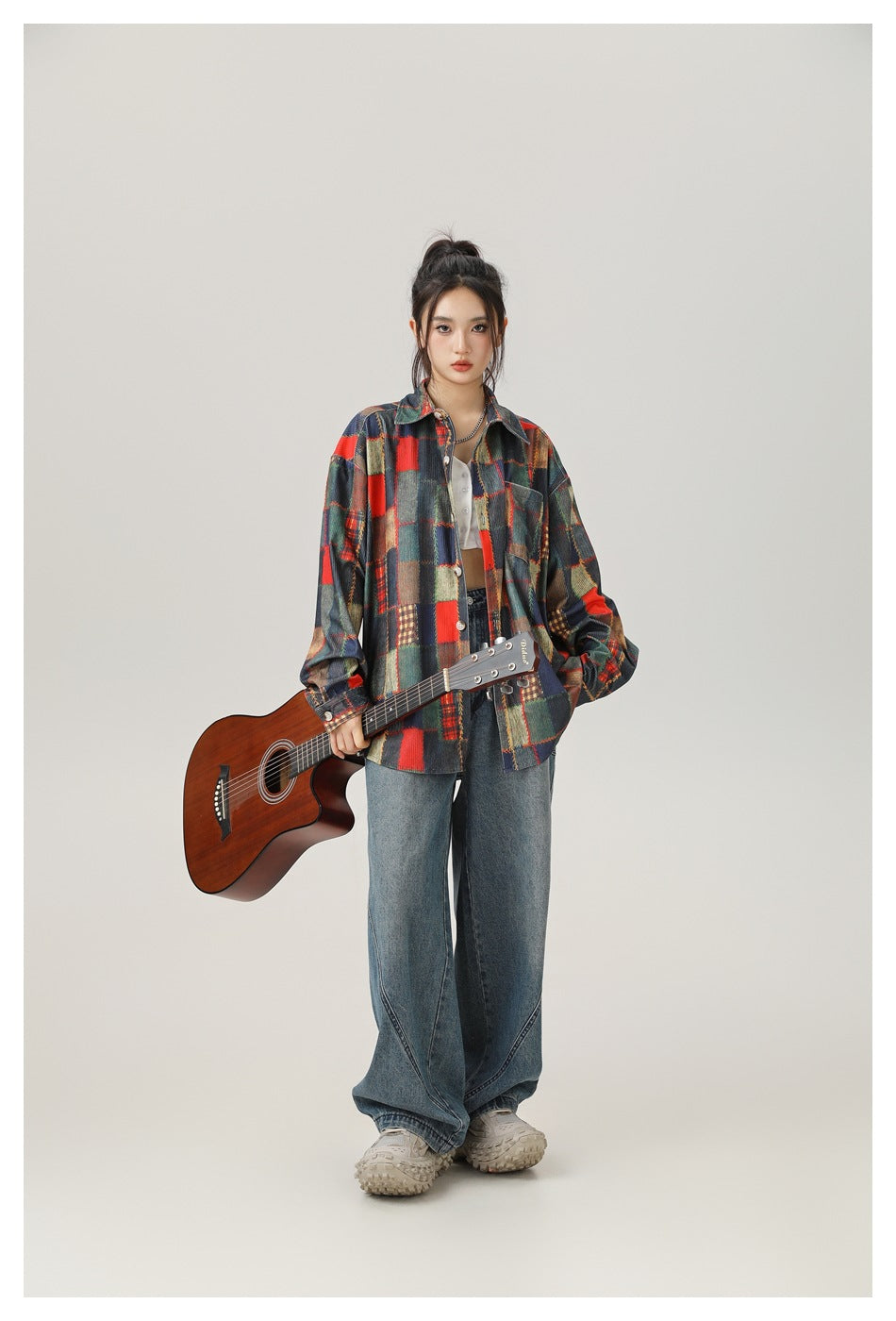 Model wearing a multicolor patchwork plaid button-up shirt and wide-leg jeans, holding a brown acoustic guitar.