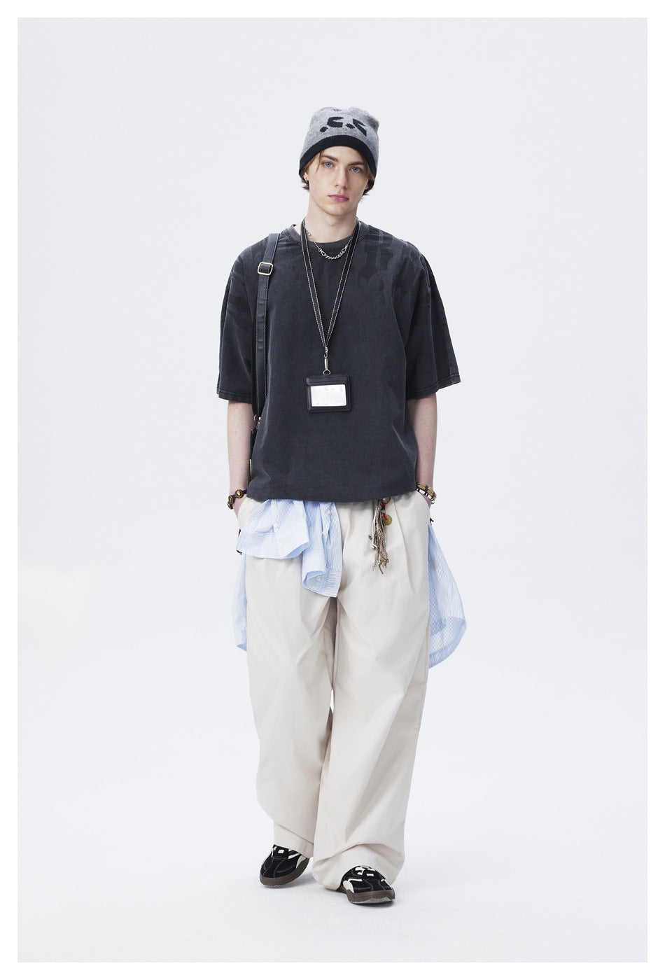 Model wearing a charcoal oversized graphic T-shirt, cream wide-leg trousers, and a gray beanie.