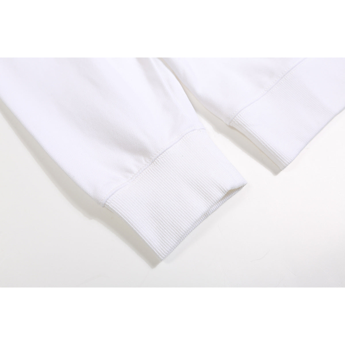 Close-up of the ribbed cuffs and sleeves of a white sweatshirt laid flat.
