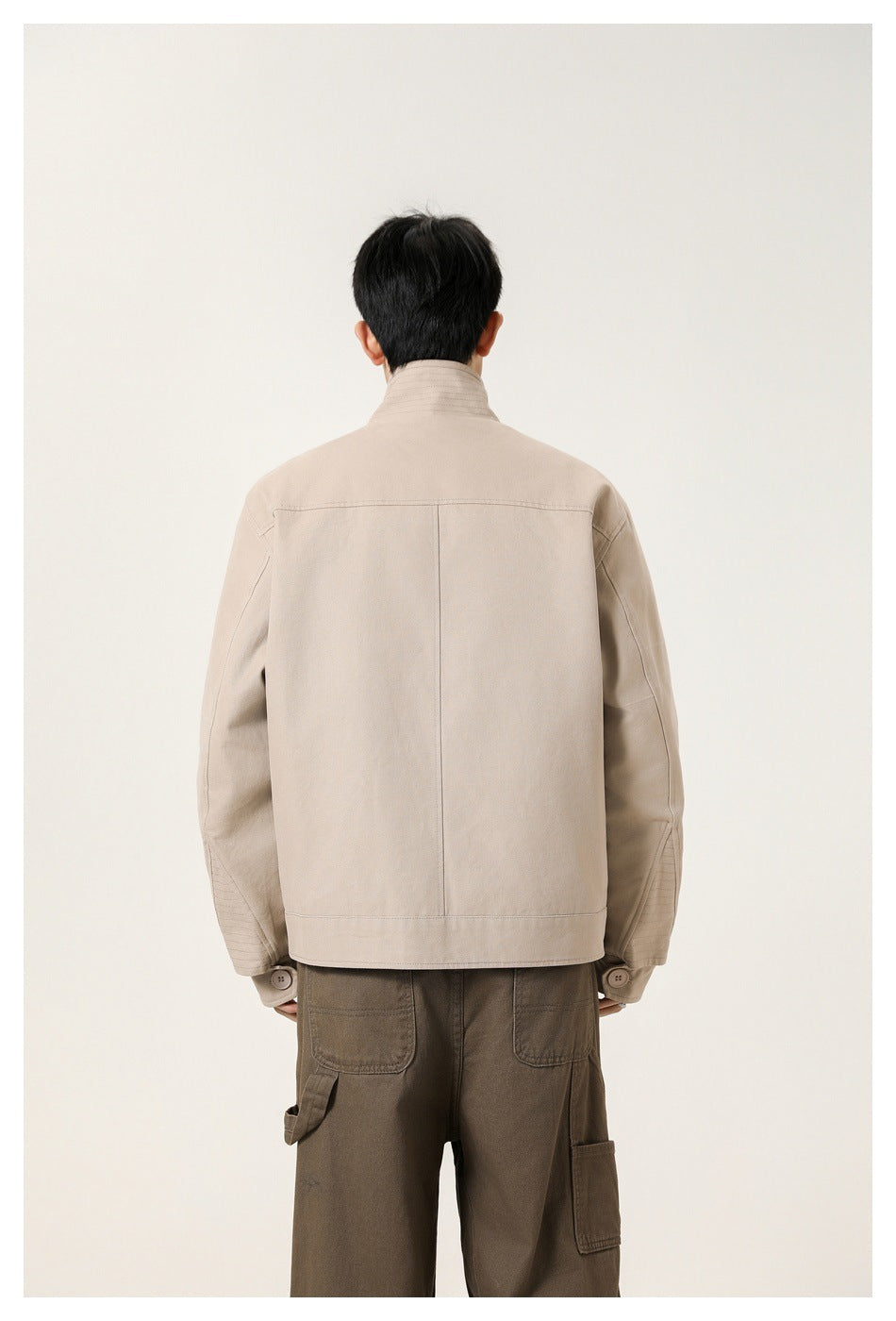 Rear view of a model wearing a beige jacket with a center back seam and buttoned cuffs.