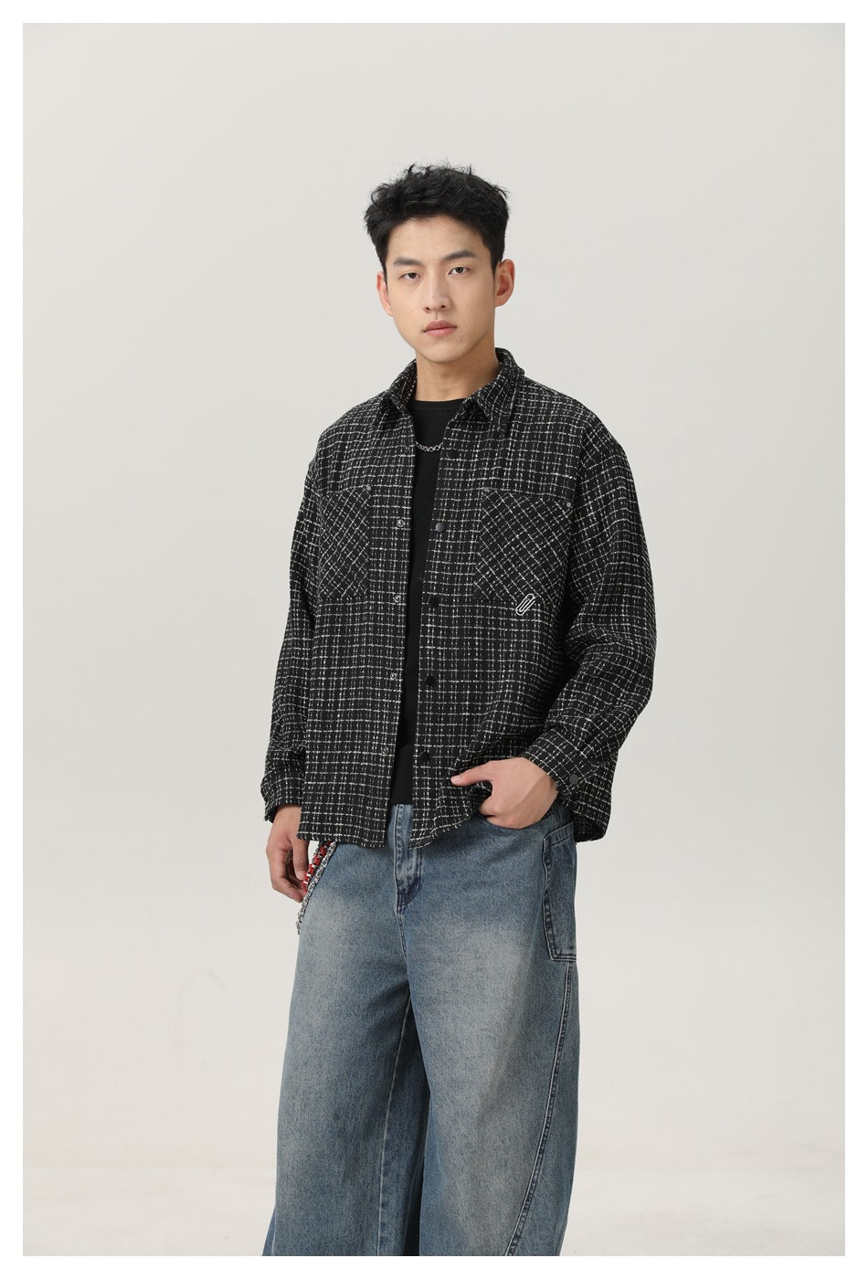 Model wearing an open black-and-white grid overshirt over a black top, with two chest pockets.