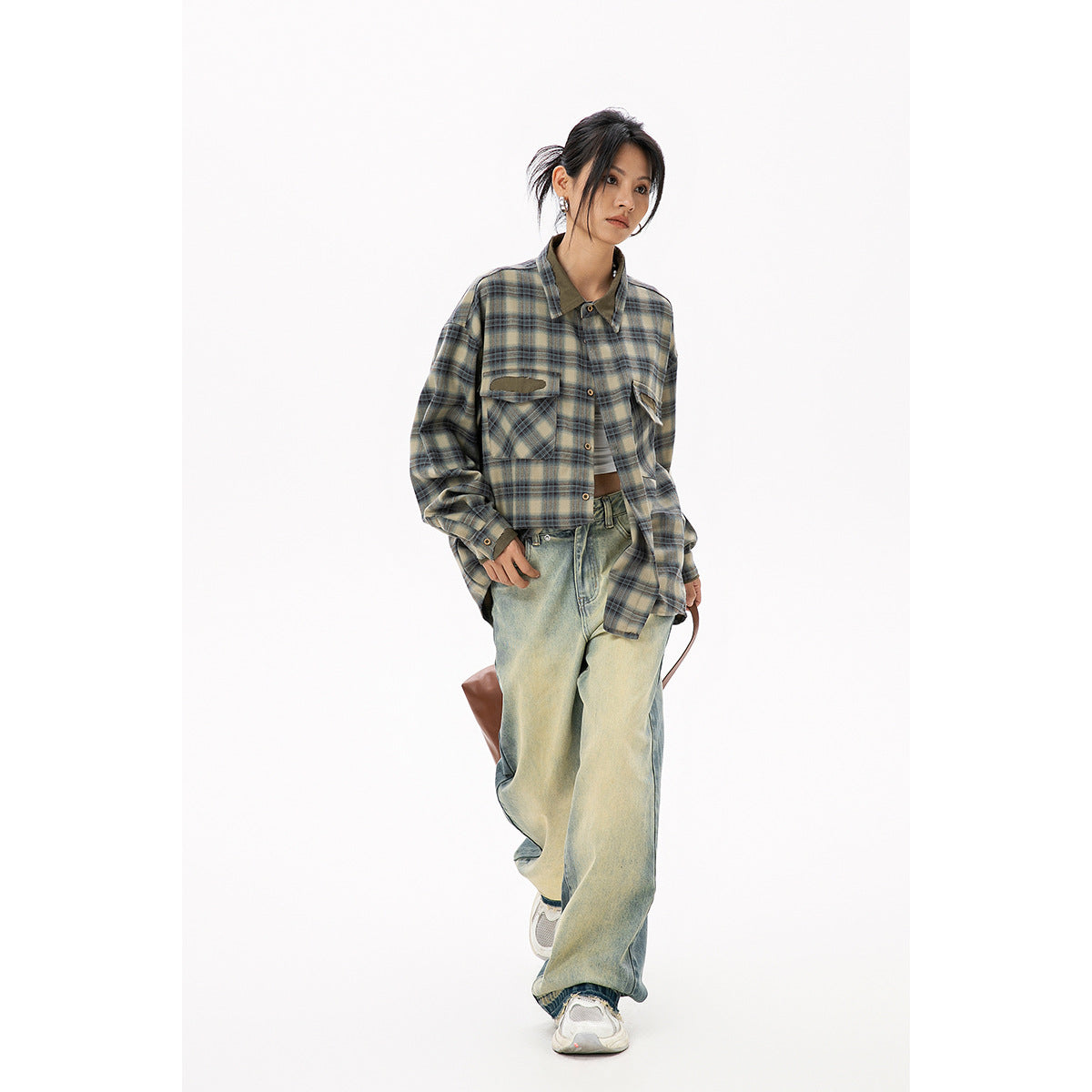 Model wearing an oversized olive and blue plaid button-up shirt with distressed chest pockets and loose faded jeans.