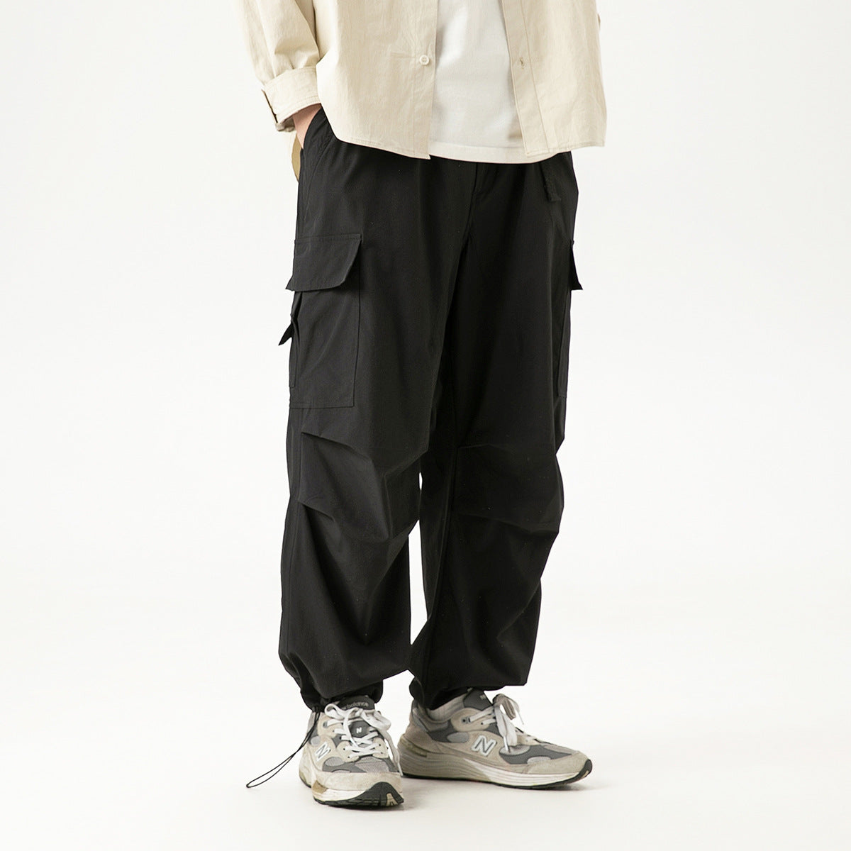 Model wearing loose black cargo pants with large flap pockets and gathered ankle cuffs, shown from the front.