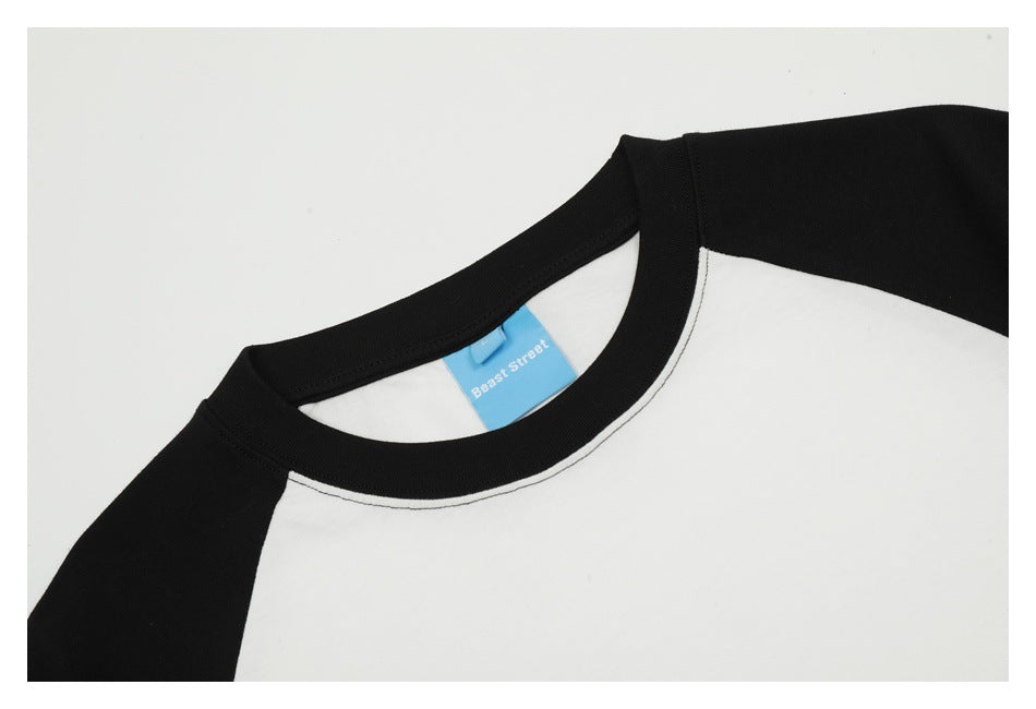 Close-up of a black crew neck and shoulder panels on a white raglan T-shirt, with a blue neck label.