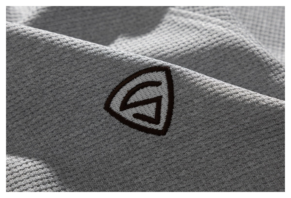 Close-up of a dark embroidered emblem on the light gray textured shirt fabric.