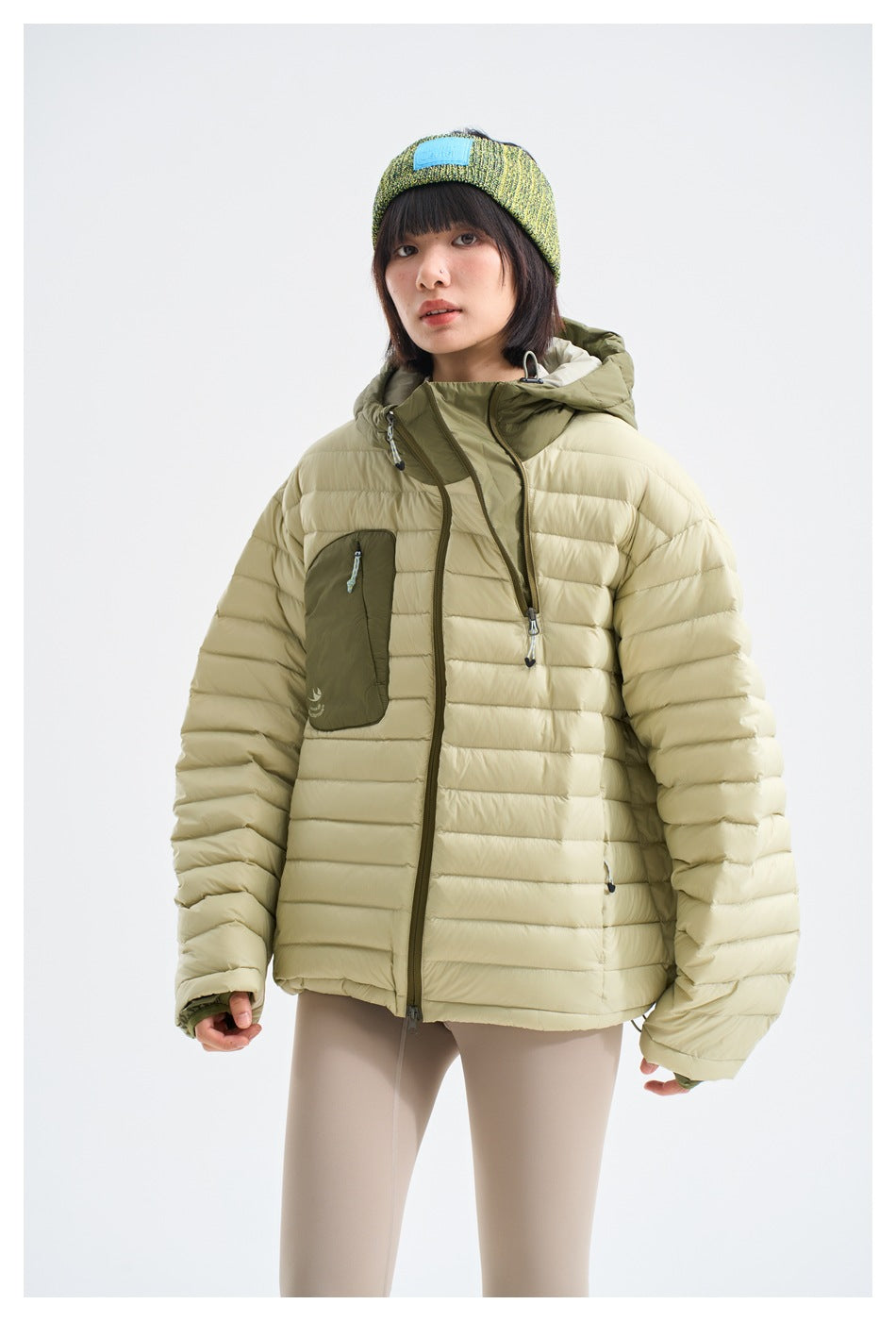 Model wearing the cream quilted jacket with its hood down, showing the olive lining, contrasting pocket and front zipper.