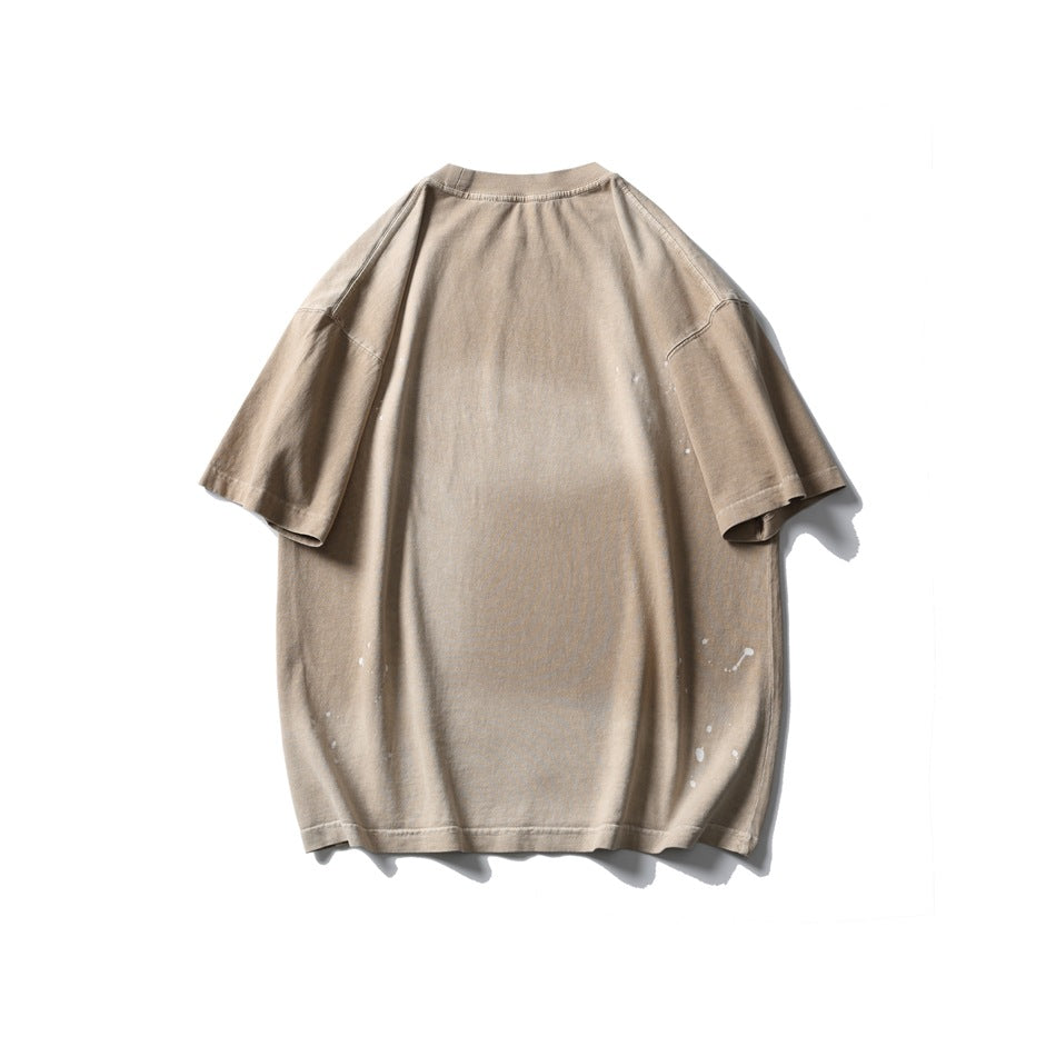 Back of an oversized light taupe short-sleeve T-shirt with small white paint-like splatters near the sides and hem.