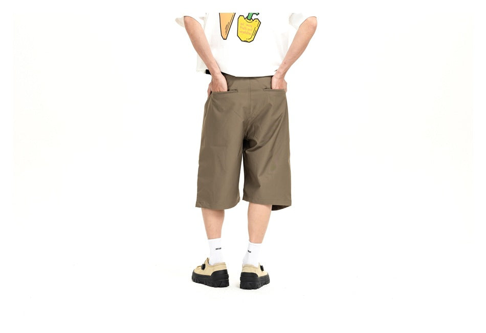 Front view of a model wearing loose olive-brown knee-length shorts with a white graphic T-shirt.