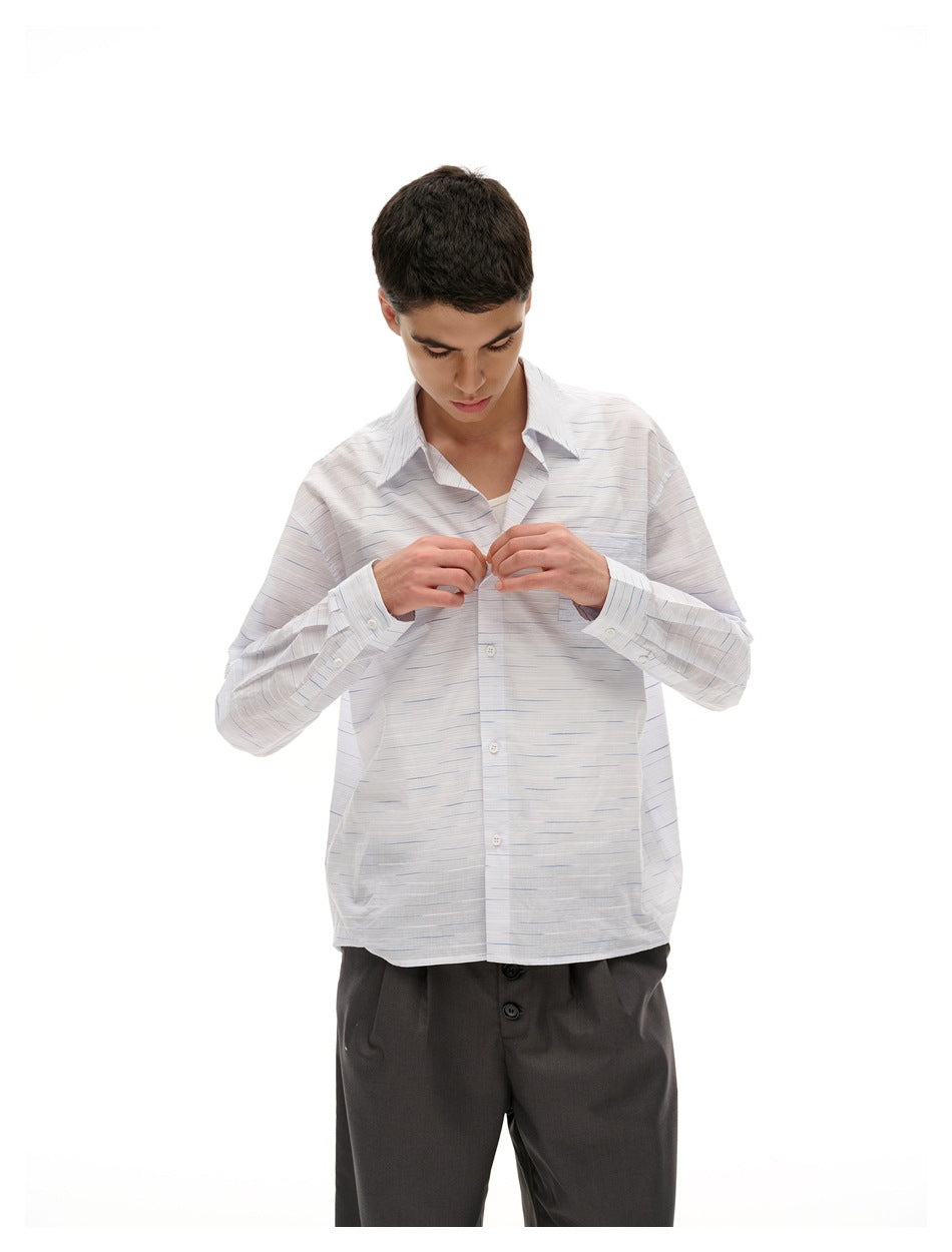 Closer view of a model buttoning a white shirt with fine blue-gray horizontal dashes and a chest pocket.