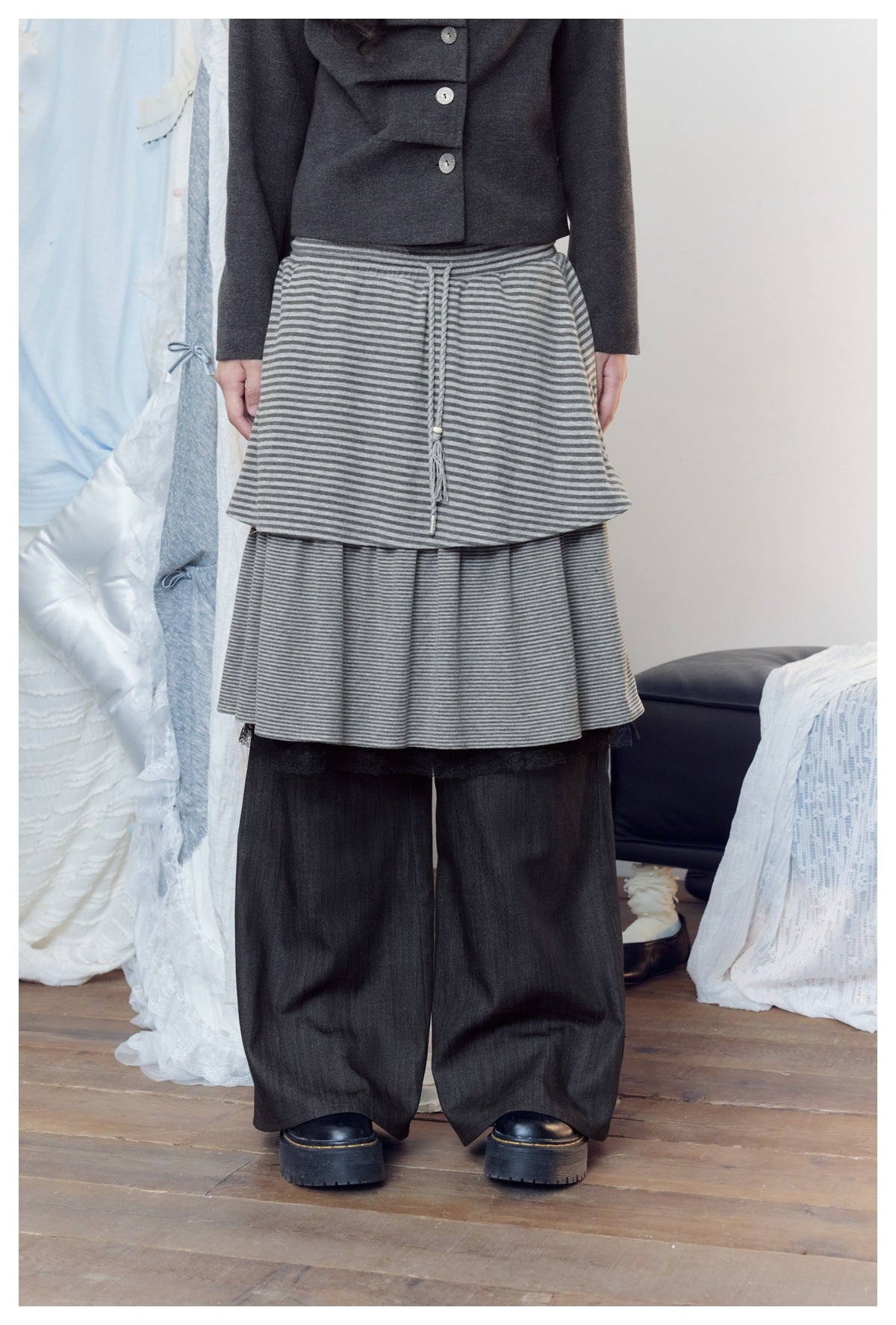 Close view of a gray striped two-tier skirt with a tasseled drawstring, layered over wide charcoal pants.
