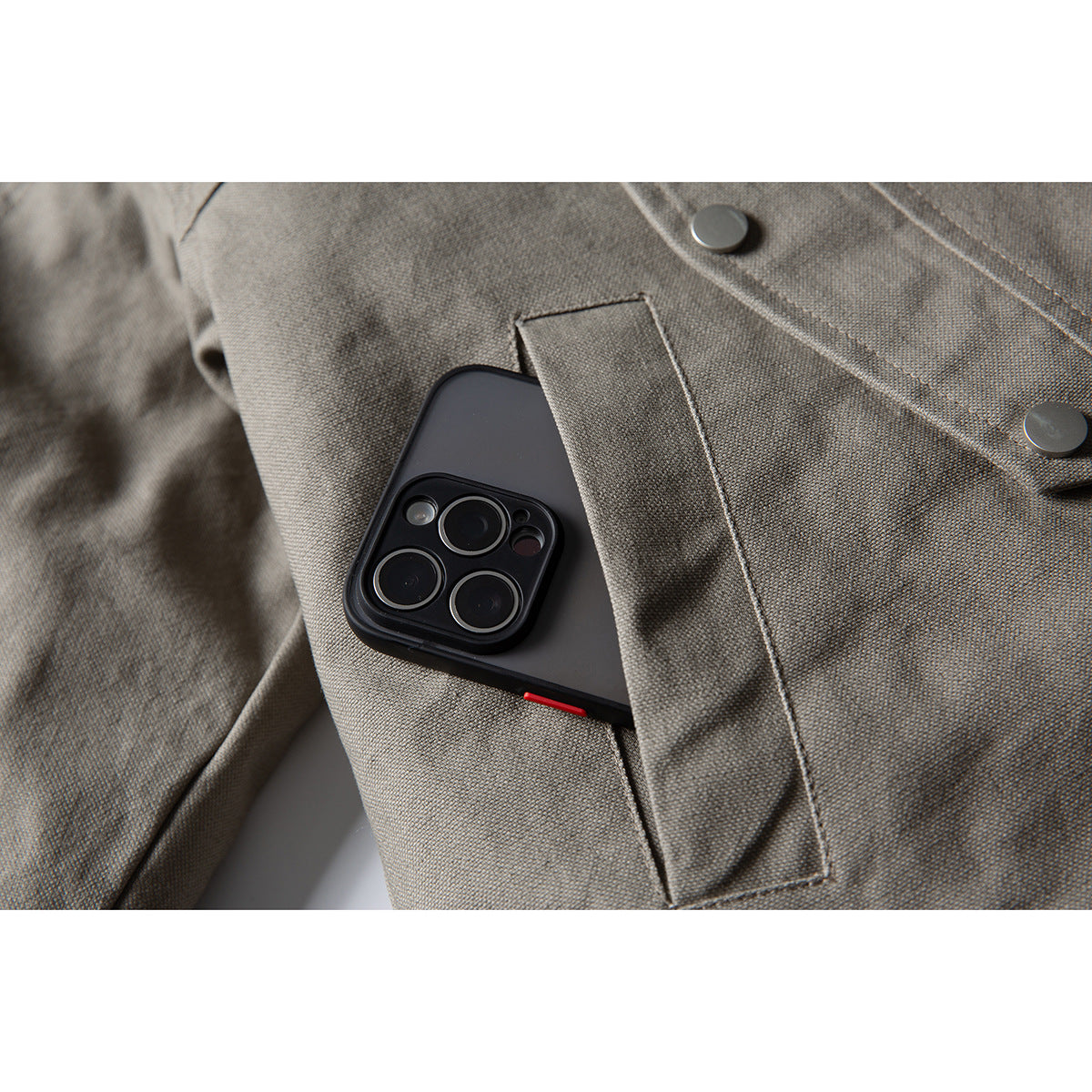 Close-up of a taupe-gray jacket pocket holding a black smartphone beneath a fabric flap.
