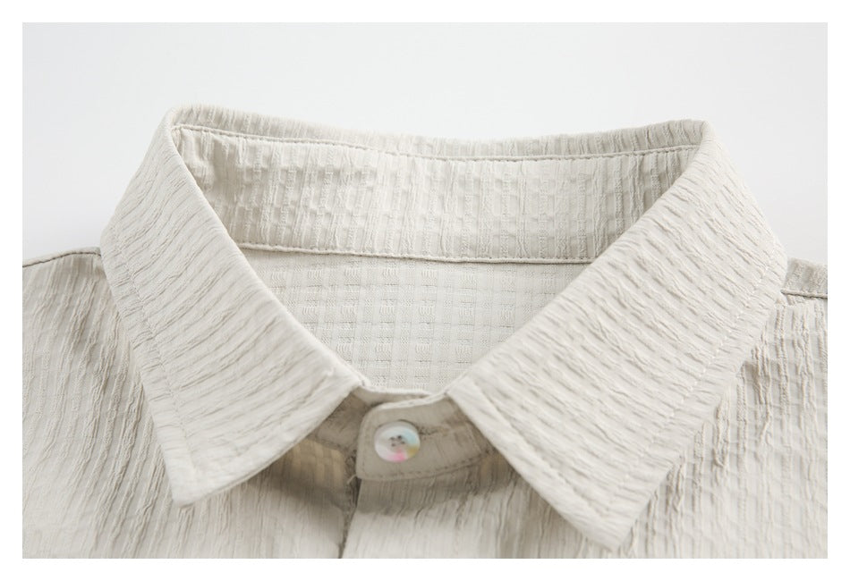 Close-up of an ivory textured shirt's pointed collar, inner collar band, and iridescent button.