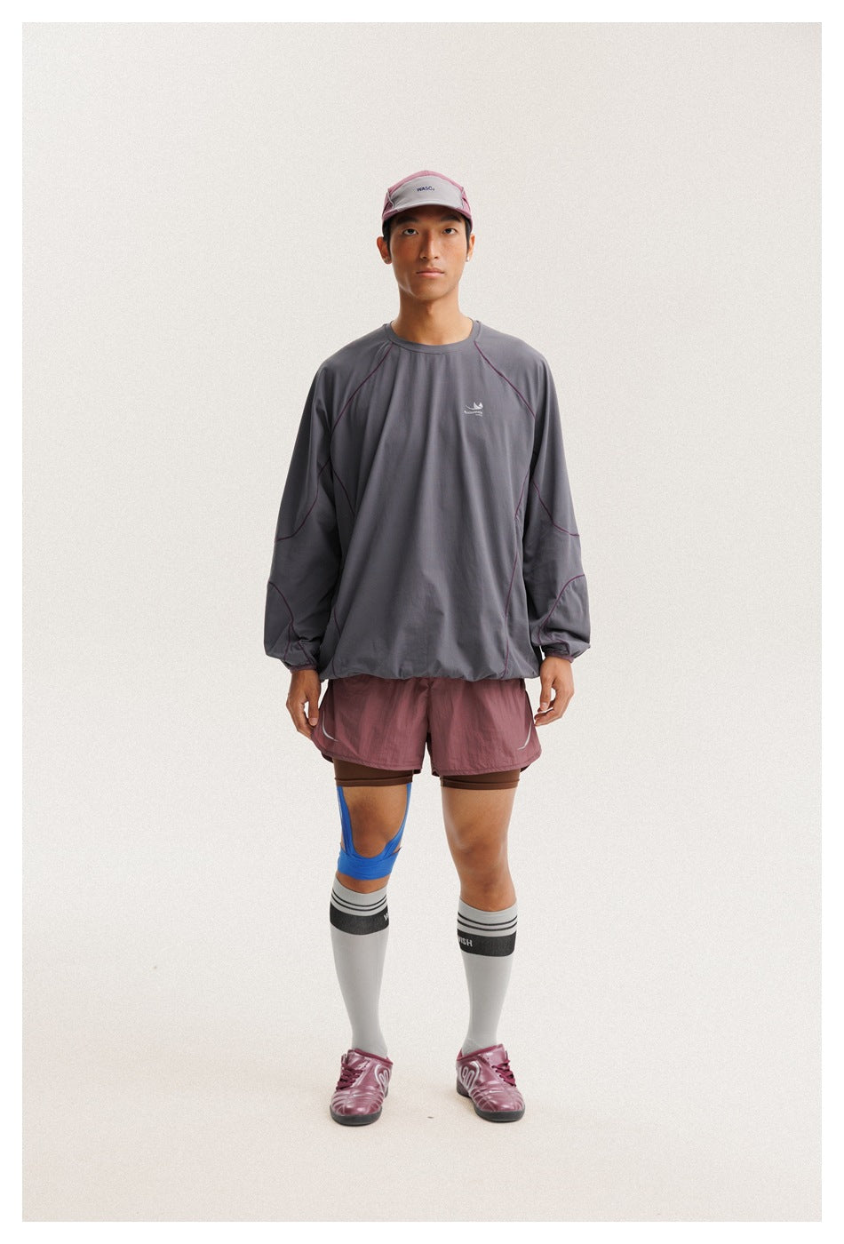 Front view of a model wearing a charcoal gray long-sleeve pullover with plum contrast seams and mauve athletic shorts.