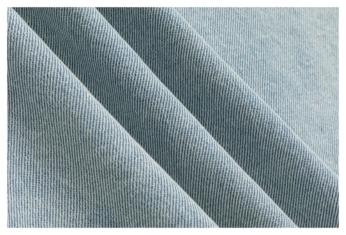 Close-up of light-blue denim fabric draped in folds, showing its diagonal weave.