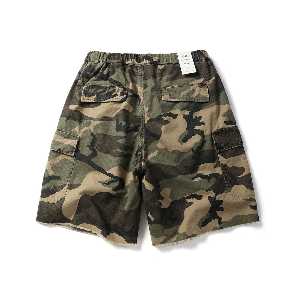 Back view of camouflage cargo shorts with an elastic waistband, flap pockets, and raw-cut hems.