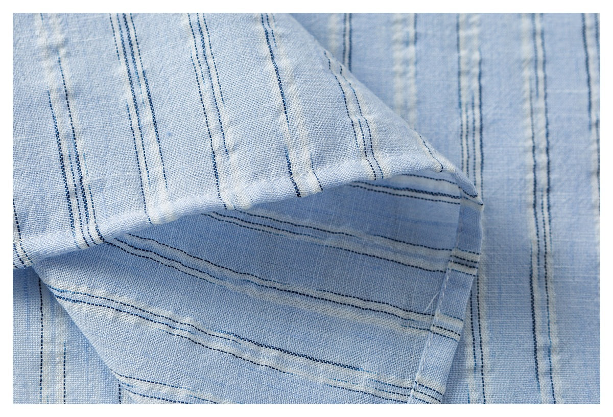 Close-up of a folded hem in pale blue fabric with narrow navy stripes and visible stitching.