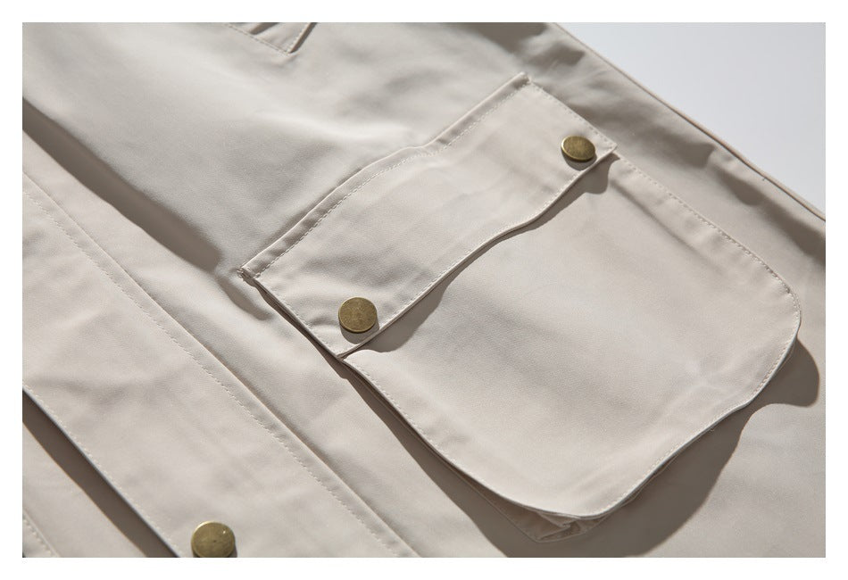 Close-up of a beige jacket's large flap pocket with two brass-tone snap buttons.