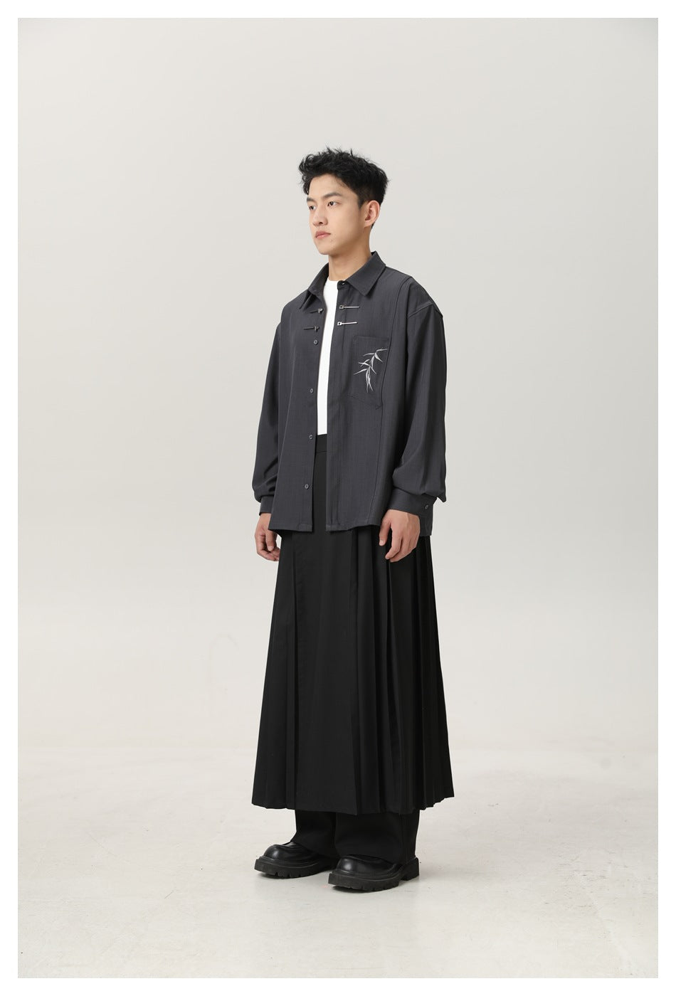 Model in dark gray shirt with bamboo pocket embroidery and black pleated bottoms, angled side view
