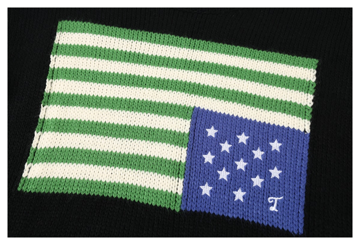 Close-up of a black knit garment with a green-and-white striped motif and a blue panel of white stars.