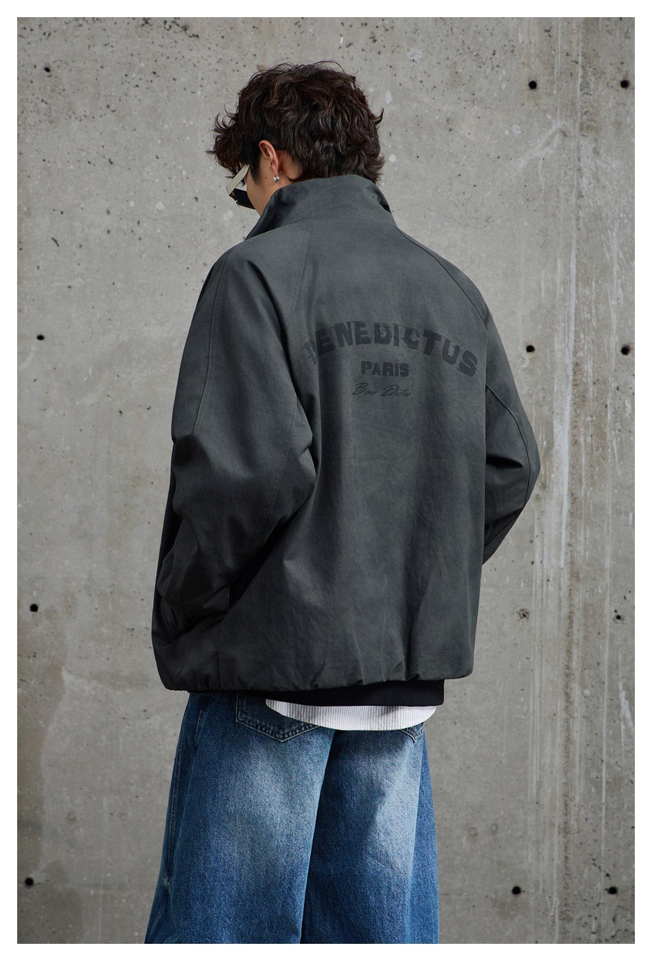 Back view of a model wearing a charcoal-gray jacket with English lettering printed across the upper back.