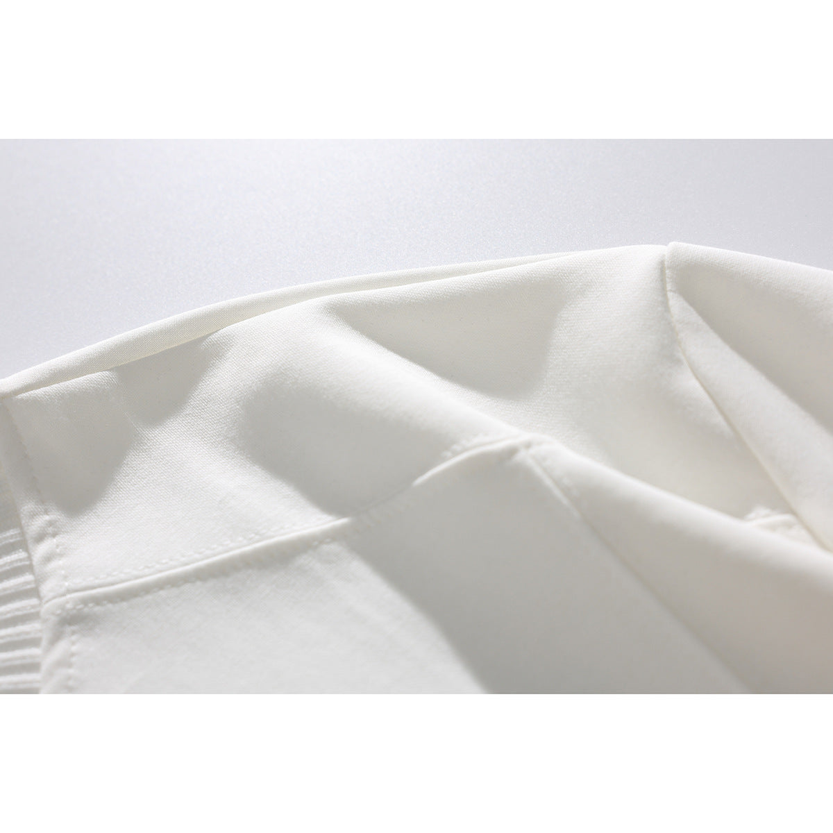 Close-up of the white T-shirt's shoulder and sleeve seams, with part of the ribbed neckline visible.