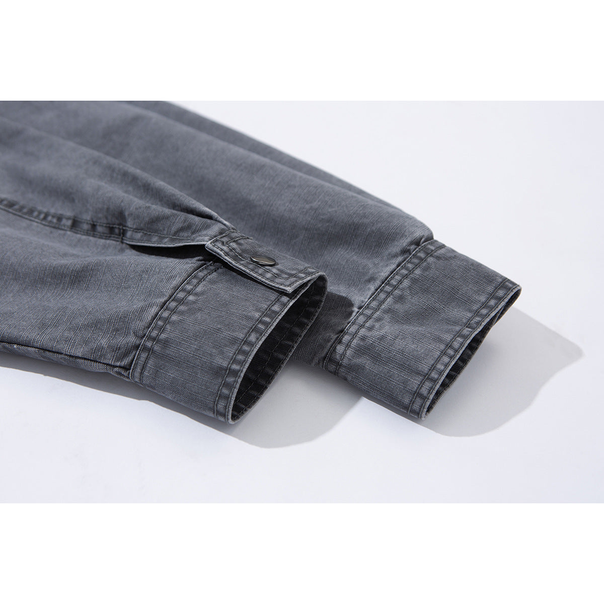 Close-up of a charcoal-gray jacket sleeve cuff with a snap button and stitched seams.