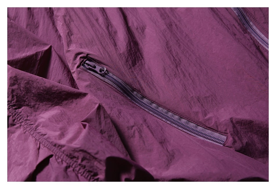 Close-up of a plum jacket showing a diagonal zippered pocket and crinkled fabric.