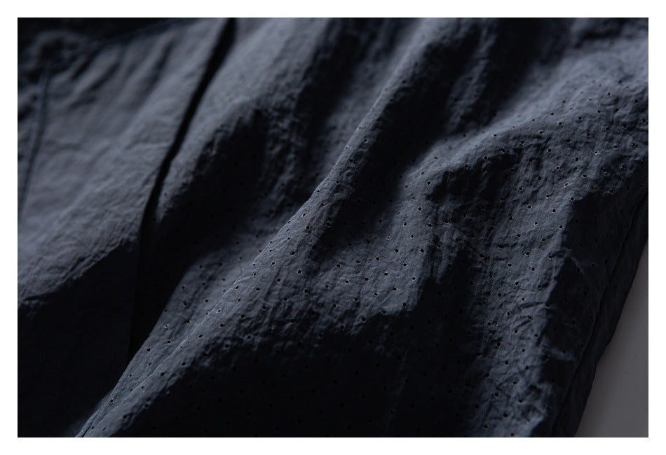 Close-up of perforated dark fabric with a crinkled surface and stitched folds.