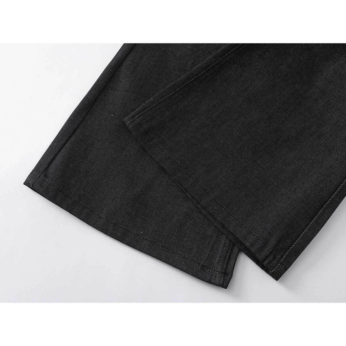 Close-up of the stitched hems on black denim pant legs.
