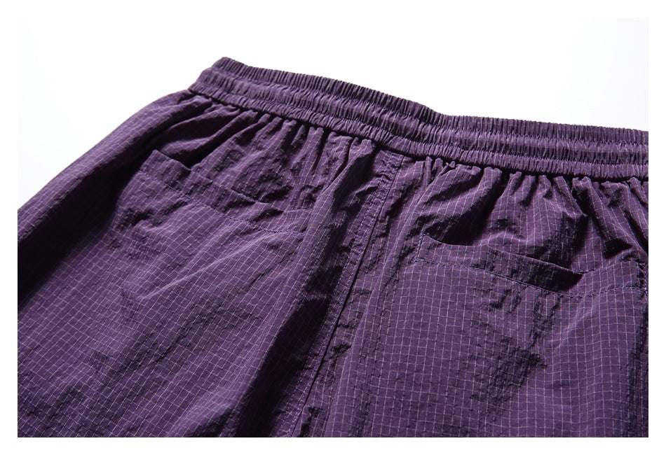 Close-up of purple grid-pattern shorts showing the gathered elastic waistband and patch pockets.