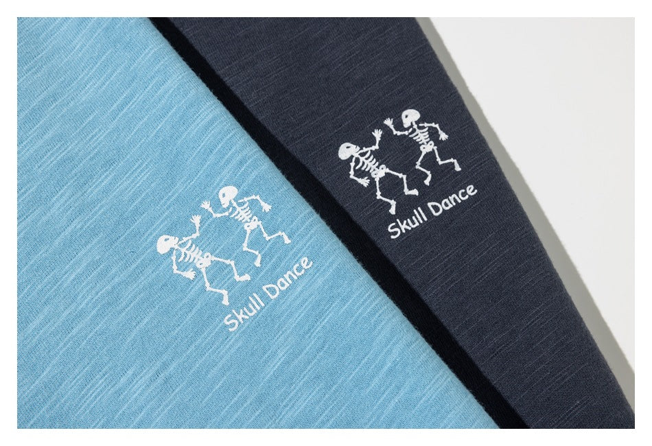Close-up of light blue and dark charcoal shirts, each printed with white dancing skeletons and “Skull Dance” text.