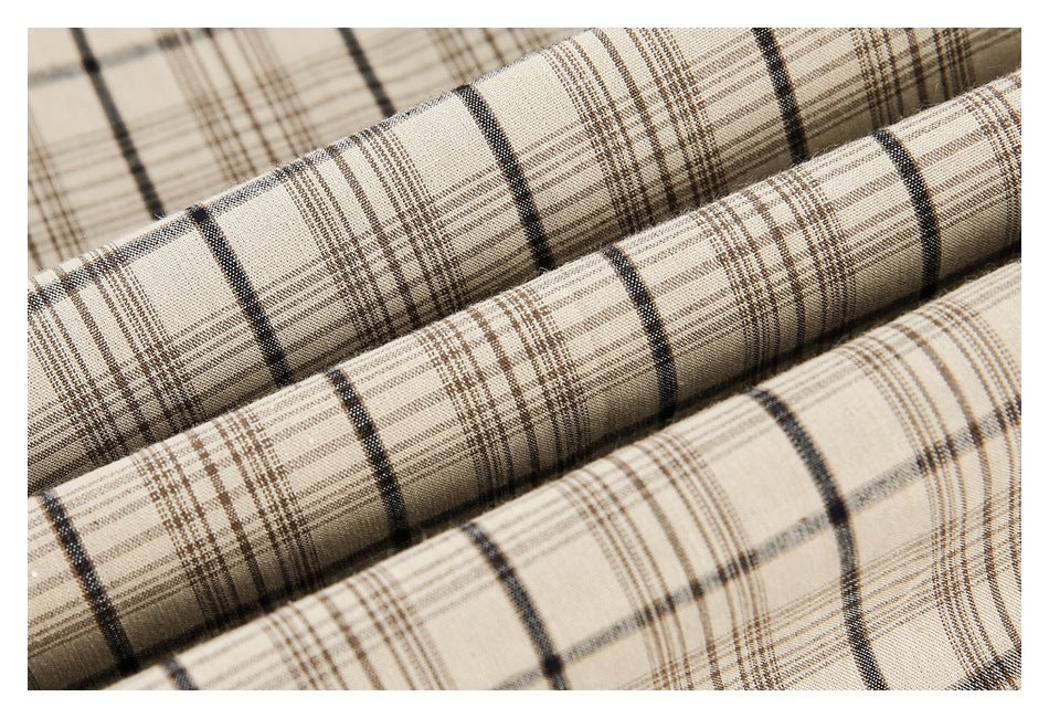 Macro view of beige fabric folded into ridges, showing its black and brown plaid pattern.
