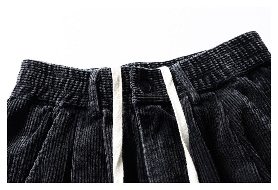 Front waistband detail of black ribbed trousers with a button, belt loops and cream drawstrings.