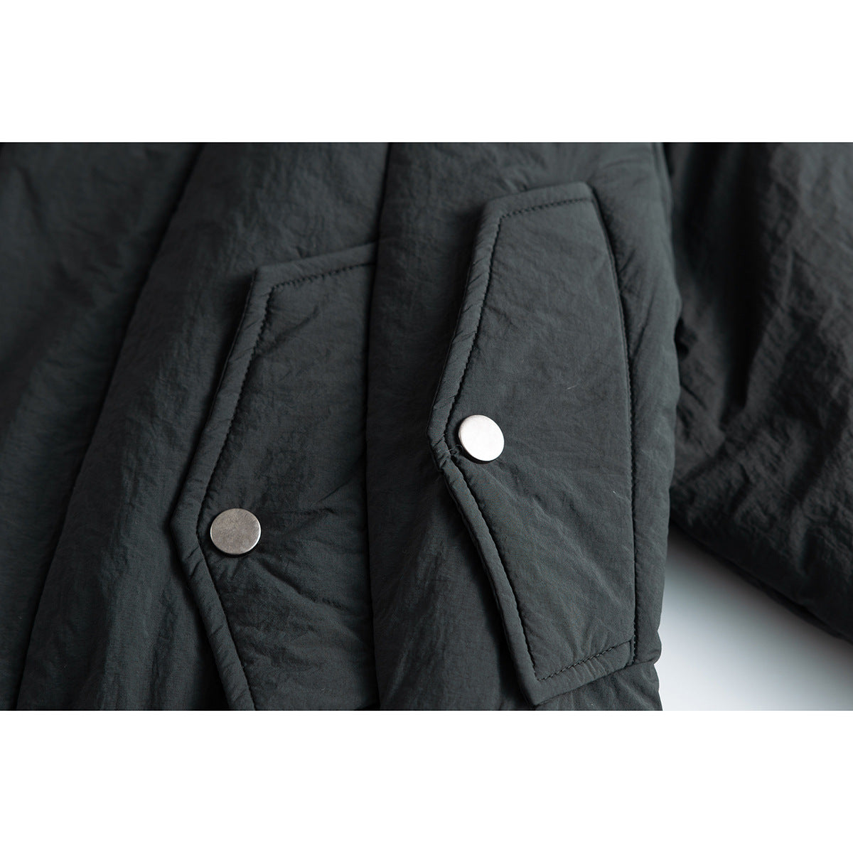 Close-up of a black jacket showing two flap pockets with round metal snap fasteners.
